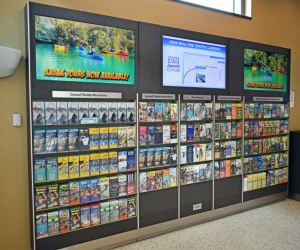 Wall brochure rack with TV screens above in plaza